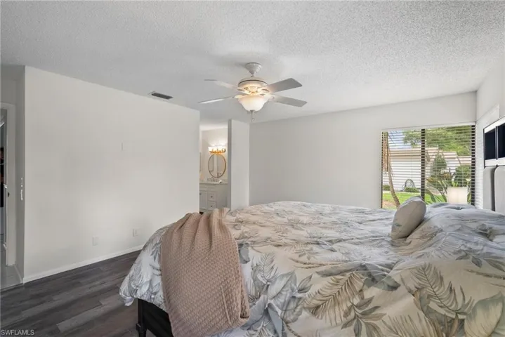 Bedroom with dark hardwood / wood-style floors, ceiling fan, connected bathroom, and a textured ceiling