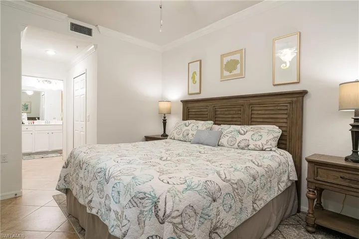 Primary bedroom featuring ensuite bath, two separate closets, ornamental molding, and light tile patterned flooring
