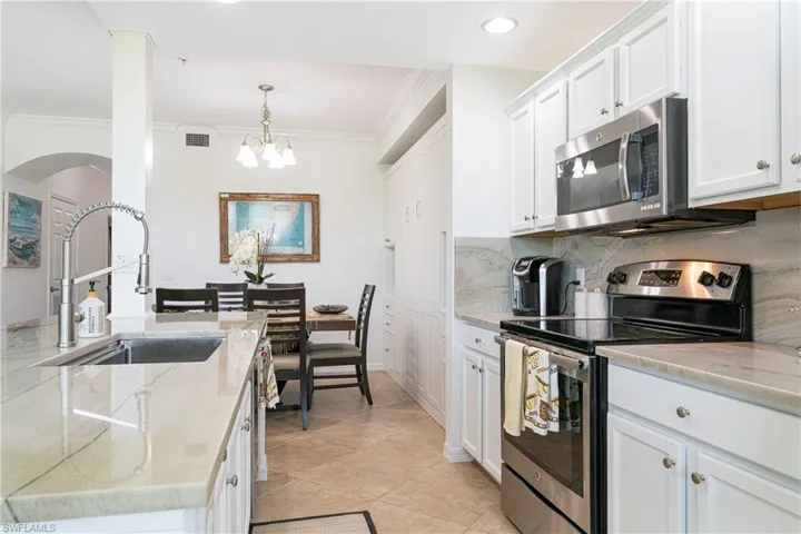 Kitchen with light stone quartzite countertops, a notable chandelier, appliances with stainless steel finishes, sink, and white cabinets