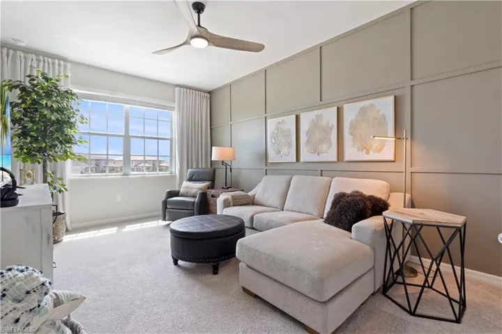 Carpeted living room with ceiling fan and a decorative wall