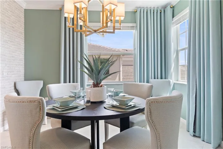 Dining area with brick wall, a chandelier, light tile patterned floors, and ornamental molding