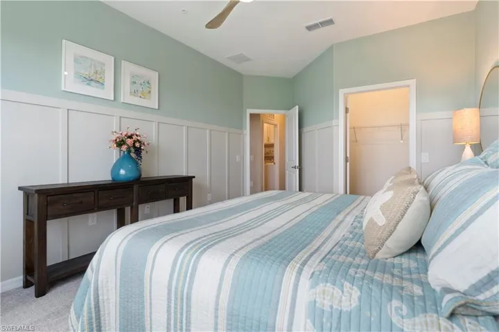 Bedroom with a decorative wall, carpet flooring, a wainscoted wall, ceiling fan, and a walk in closet