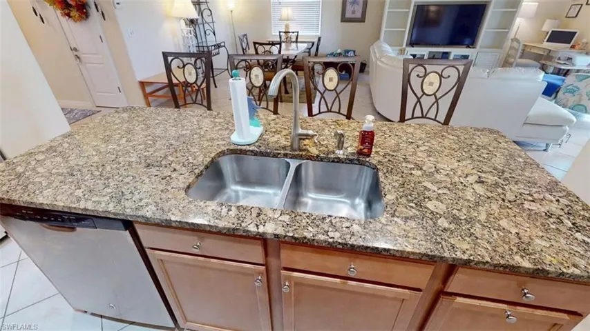 Kitchen with light tile patterned floors, an island with sink, open floor plan, stainless steel dishwasher, and light stone countertops