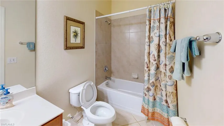Bathroom featuring shower / bath combo with shower curtain, vanity, tile patterned floors, and a textured wall