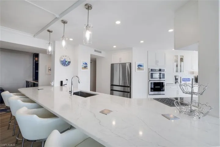 Kitchen with appliances with stainless steel finishes, a sink, light stone countertops, a kitchen bar, and white cabinetry