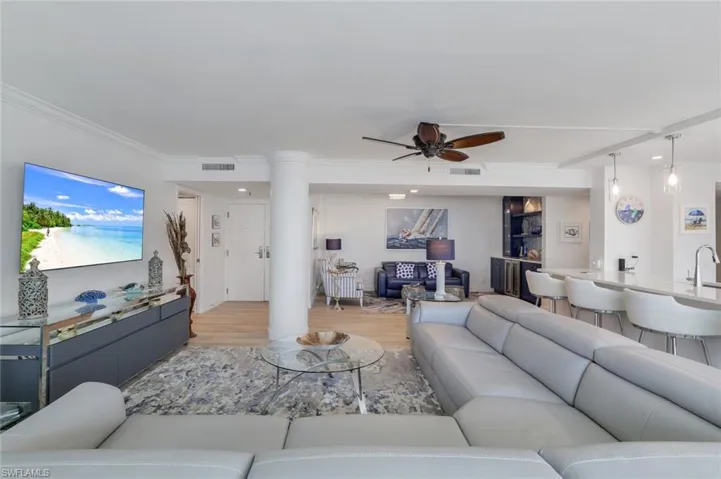 Living area with ceiling fan, light wood-style floors, ornate columns, and ornamental molding