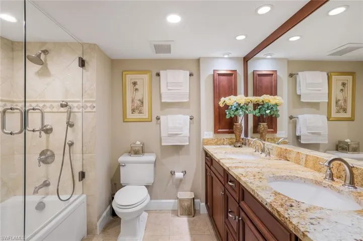Full bath with baseboards, double vanity, recessed lighting, toilet, and bath / shower combo with glass door
