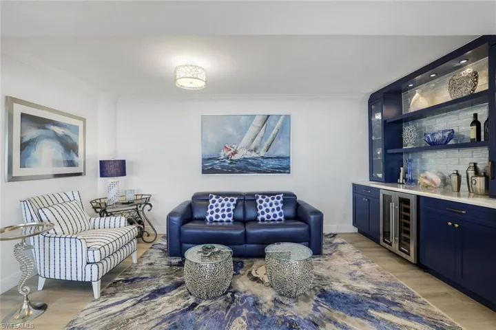 Living area with beverage cooler, ornamental molding, bar area, light wood-style floors, and baseboards