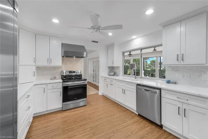 Kitchen with white cabinetry, stainless steel appliances, ceiling fan, wall chimney exhaust hood, and light hardwood / wood-style floors