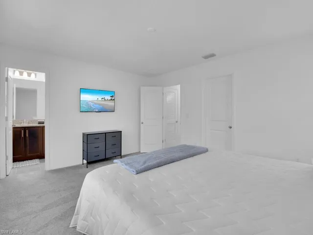 Bedroom with ensuite bathroom, visible vents, and carpet floors