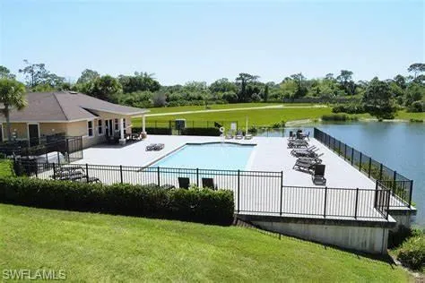 Pool featuring a lawn, a water view, fence, and a patio area