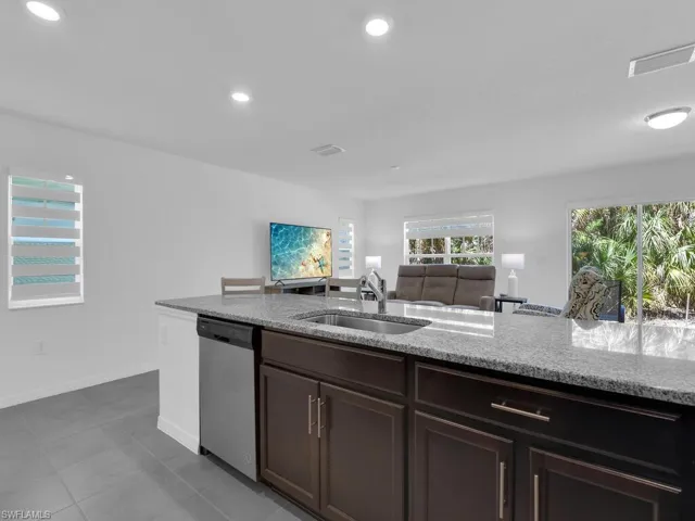 Kitchen featuring recessed lighting, stainless steel dishwasher, a sink, light stone counters, and dark brown cabinets