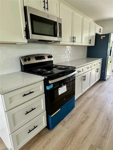 Kitchen with light stone counters, light hardwood / wood-style floors, tasteful backsplash, white cabinetry, and appliances with stainless steel finishes