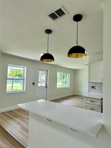 Kitchen with tasteful backsplash, light wood-type flooring, pendant lighting, light stone counters, and white cabinets
