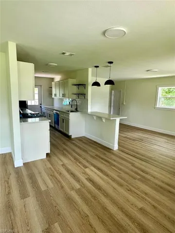 Kitchen with dishwasher, a kitchen breakfast bar, hanging light fixtures, light wood-type flooring, and sink