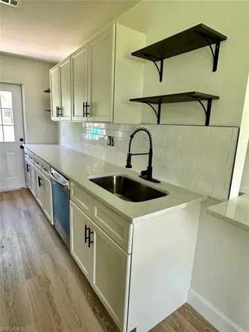 Kitchen featuring stainless steel dishwasher, light wood-type flooring, backsplash, sink, and white cabinetry