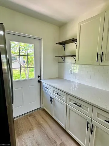 Kitchen with backsplash, stainless steel refrigerator, light stone countertops, and light wood-type flooring