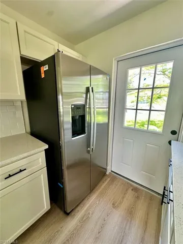 Kitchen featuring white cabinetry, light hardwood / wood-style flooring, light stone counters, backsplash, and stainless steel refrigerator with ice dispenser