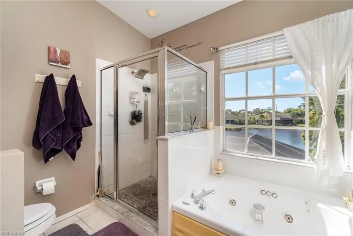 Bathroom featuring toilet, a water view, a healthy amount of sunlight, and separate shower and tub