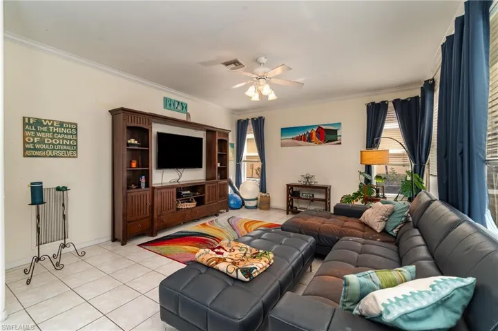Living room featuring ornamental molding, ceiling fan, and light tile patterned floors