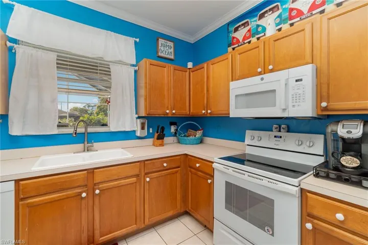 Kitchen featuring white appliances, crown molding, sink, and light tile patterned floors