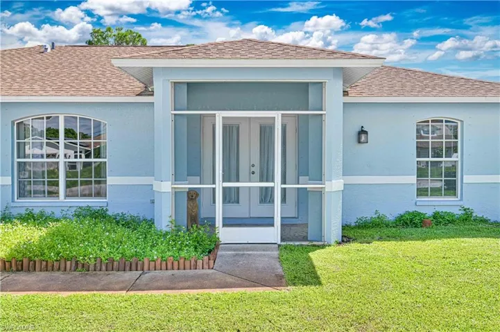 Property entrance featuring roof with shingles, a lawn, stucco siding, and french doors