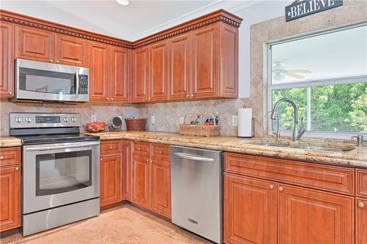 Kitchen with appliances with stainless steel finishes, backsplash, ornamental molding, light stone counters, and brown cabinetry
