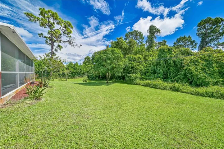 View of grassy yard featuring a sunroom and view of wooded area
