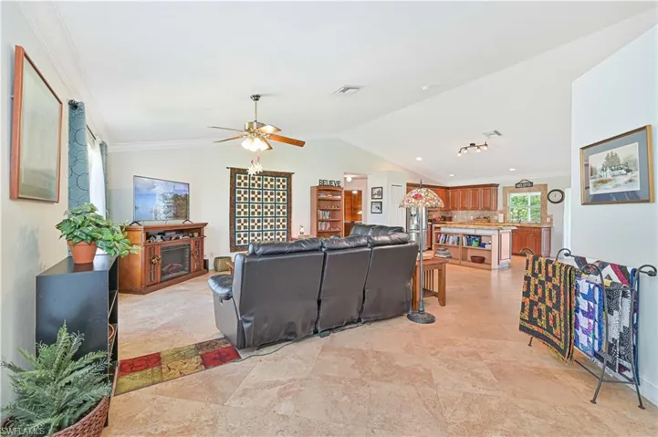 Living room featuring crown molding, lofted ceiling, ceiling fan, and a fireplace
