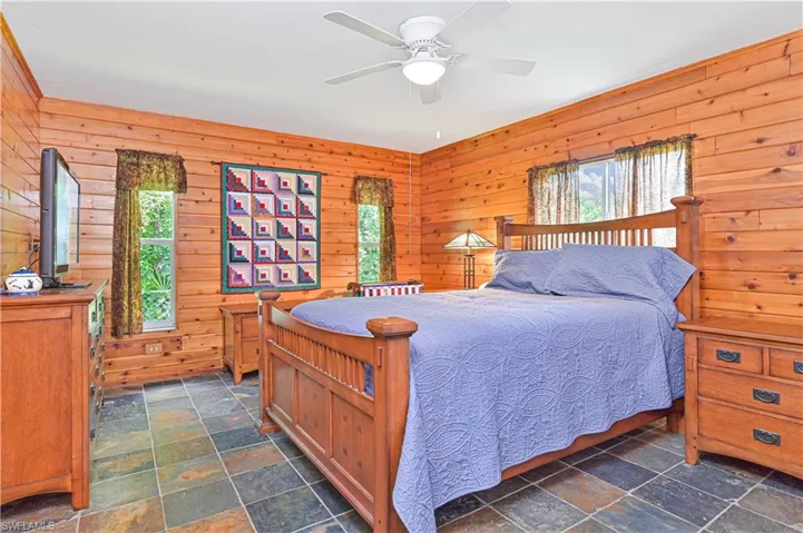 Bedroom featuring wood walls, stone tile floors, and a ceiling fan