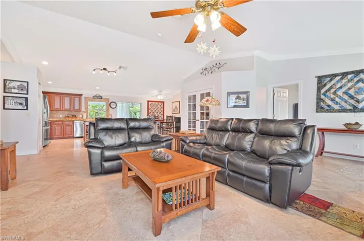 Living area with ornamental molding, vaulted ceiling, ceiling fan, recessed lighting, and french doors