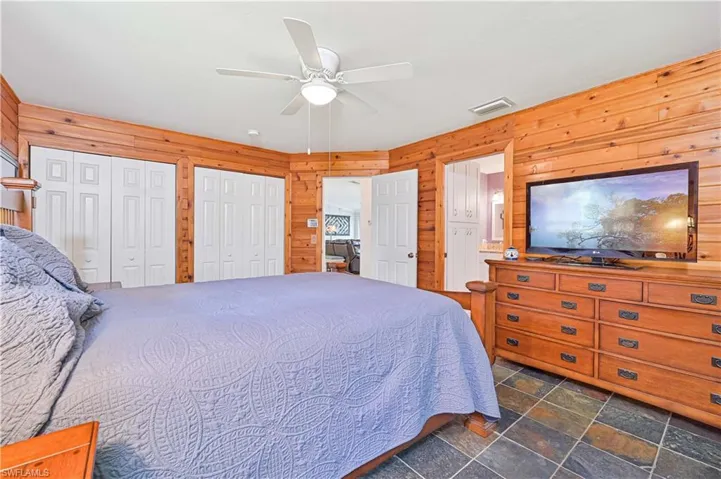 Bedroom featuring wooden walls, multiple closets, stone tile floors, and a ceiling fan