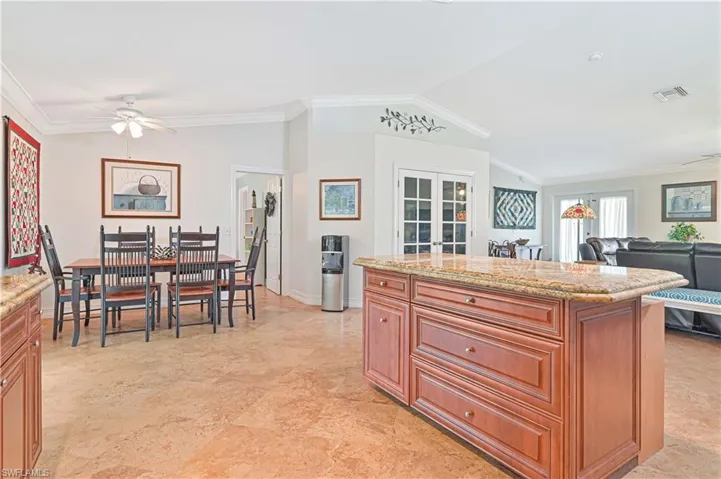 Kitchen featuring a ceiling fan, crown molding, light stone counters, lofted ceiling, and a center island