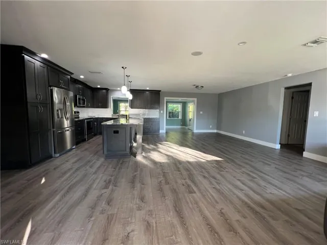 Kitchen featuring dark wood-type flooring, tasteful backsplash, decorative light fixtures, a kitchen island, and stainless steel appliances