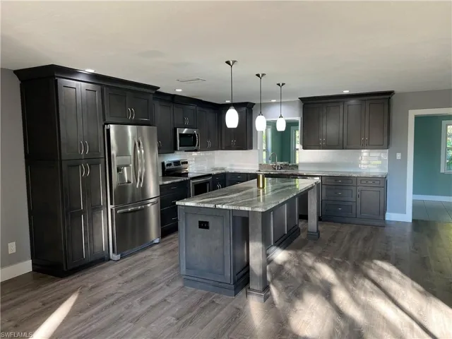 Kitchen featuring a kitchen bar, light stone counters, hanging light fixtures, appliances with stainless steel finishes, and a kitchen island