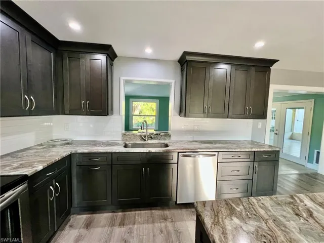 Kitchen with stainless steel appliances, sink, decorative backsplash, and light wood-type flooring