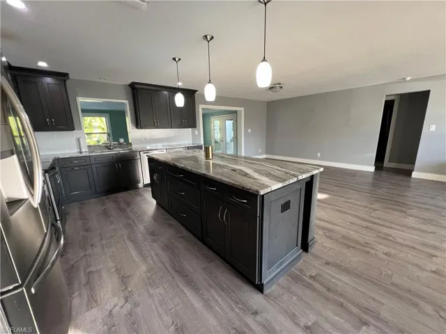 Kitchen featuring light stone counters, wood-type flooring, decorative light fixtures, a center island, and stainless steel appliances