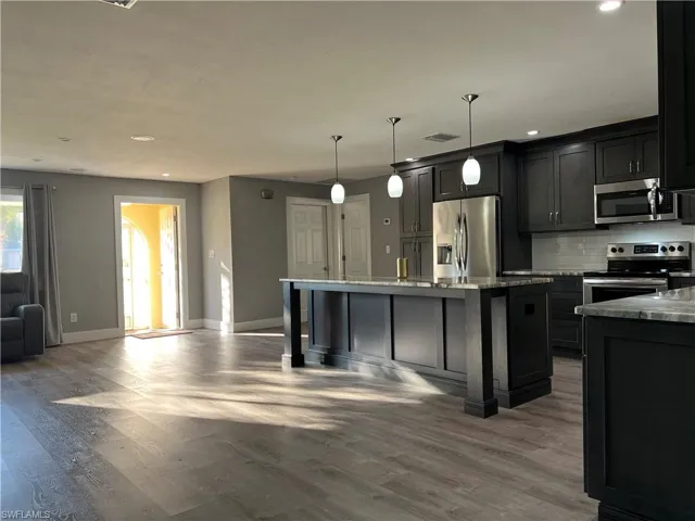 Kitchen with hanging light fixtures, appliances with stainless steel finishes, a center island with sink, and light stone counters