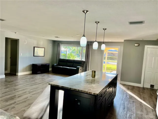 Kitchen with decorative light fixtures, wood-type flooring, light stone countertops, and a center island