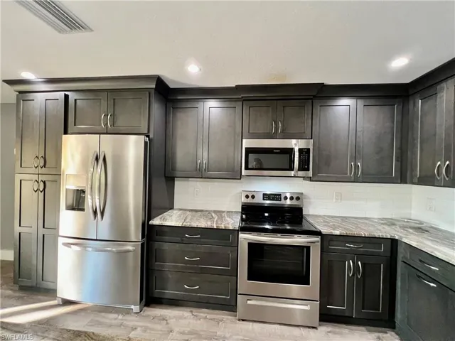 Kitchen featuring tasteful backsplash, light stone countertops, appliances with stainless steel finishes, and light wood-type flooring