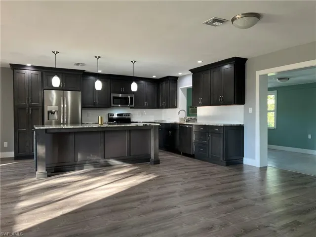 Kitchen featuring appliances with stainless steel finishes, decorative light fixtures, sink, backsplash, and dark wood-type flooring