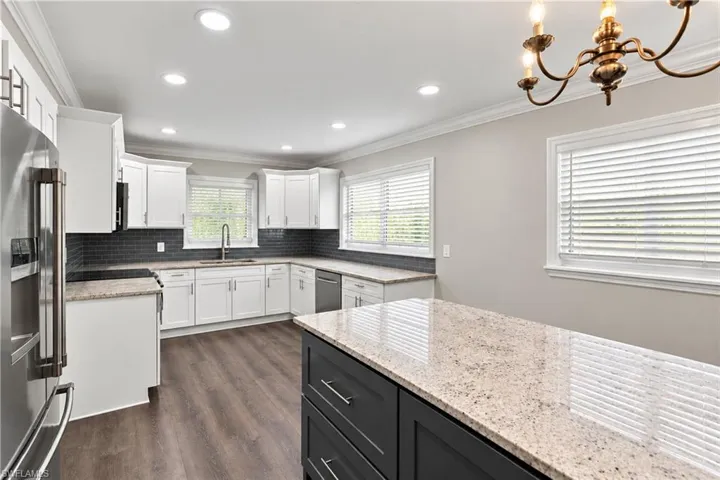 Modern kitchen featuring white cabinetry, dark gray subway tile backsplash, granite countertops, and wood-finish flooring - All matching stainless steel appliances- Crown molding to cabinets as well as in the ceiling- Multiple in-ceiling can lights, large master island with additional storage virtually adjust a picture to remove personal items.