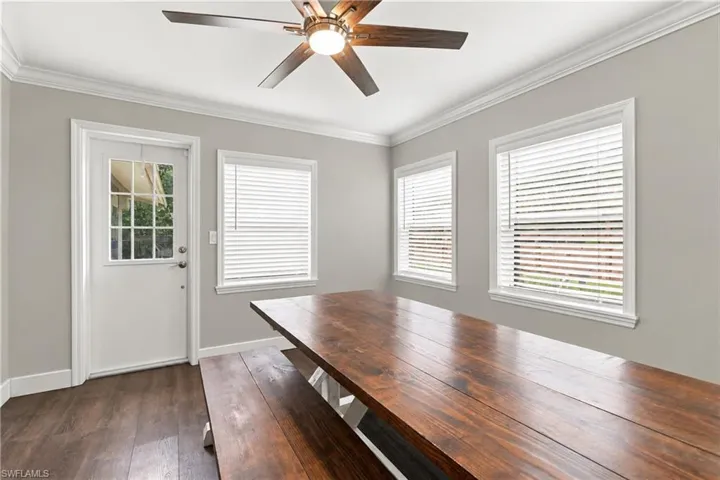 Room featuring wood-finish flooring, two windows with blinds, a ceiling fan with integrated lighting, a white panel door with glass inserts, and crown molding