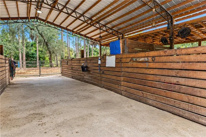 Covered equestrian facility featuring a durable metal roof and robust wooden stalls as well as gates at the beginning and ending of the stable