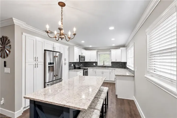 Kitchen featuring white cabinetry, stainless steel appliances, granite countertops, and wood-finish flooring