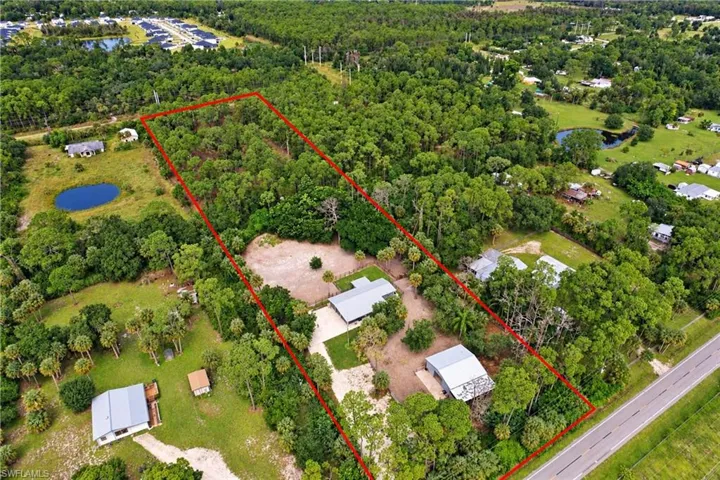 Expansive wooded lot with multiple structures, including a primary residence with a gray roof and a separate outbuilding with a metal roof back two pastures separated from front two pastures via small stream