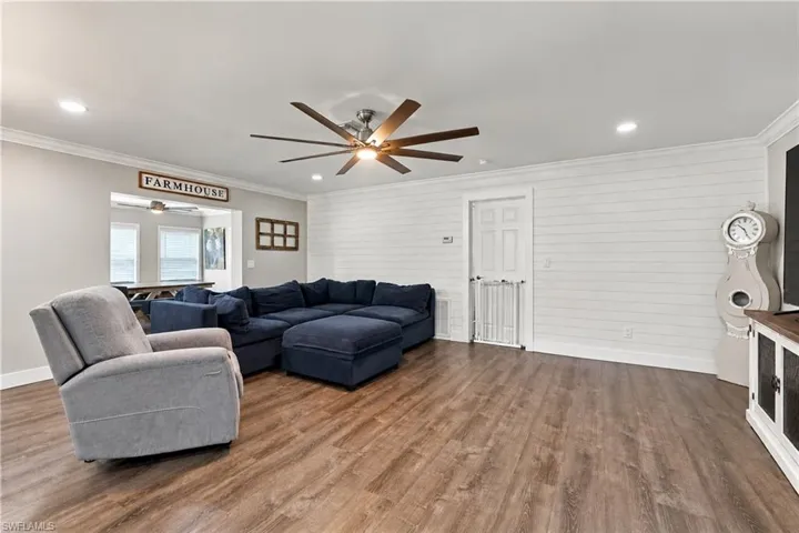 Wood-finish flooring throughout, white shiplap accent wall, overhead ceiling fan with lighting, recessed ceiling lighting, and crown molding virtually adjusted pictures to remove personal items.