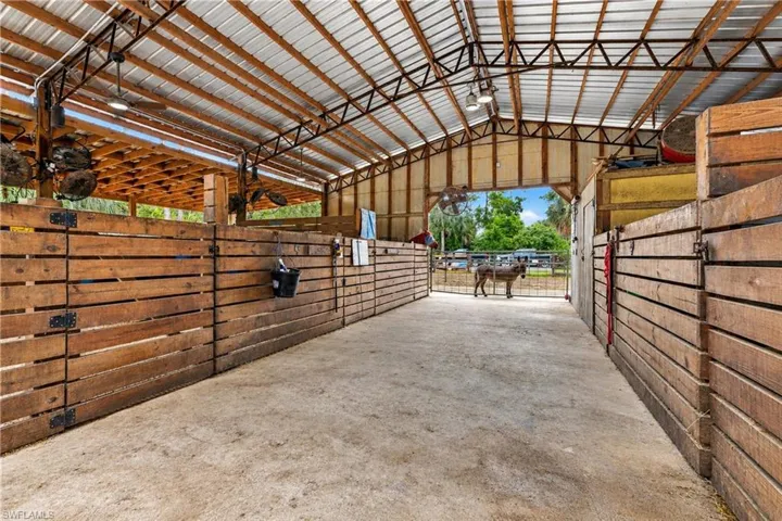 Sturdy wood-slat stalls, exposed metal beam structure, corrugated metal roofing, built-in overhead lighting, and concrete flooring