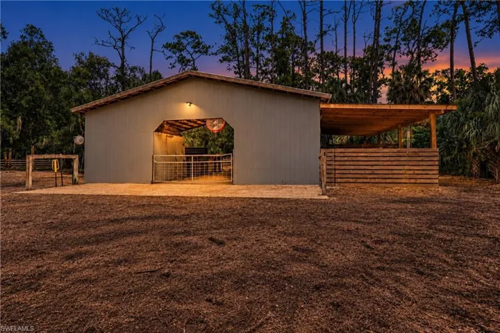 Barn structure featuring a covered entrance, exterior lighting, and an attached open-air wood-framed lean-to. Two hitching posts and a washing station on an expansive contract entrance patio to a barn .