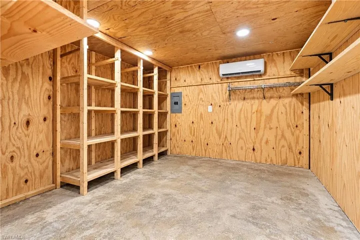 Plywood-paneled walls and ceiling, built-in wooden shelving, concrete flooring, recessed lighting, and wall-mounted climate control unit virtually adjusted picture to show layout and spacing of tack room.